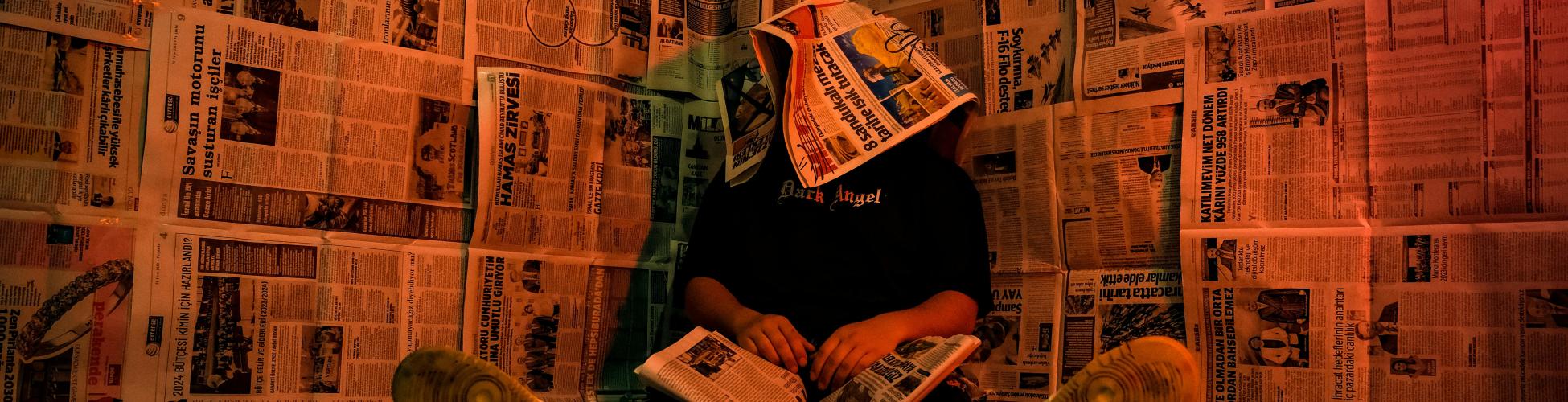 Photo artistique d'une personne assise dans une pièce recouverte de papier journal
